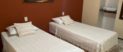 Two single beds with white bedding in a room with a red wall and a painting of a sunset.