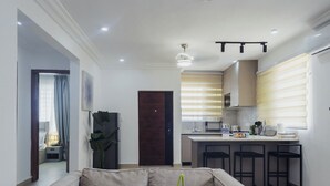 Una sala de estar moderna con un sofá y una planta de orquídea, que da a una cocina con barra y una mesa de comedor.
