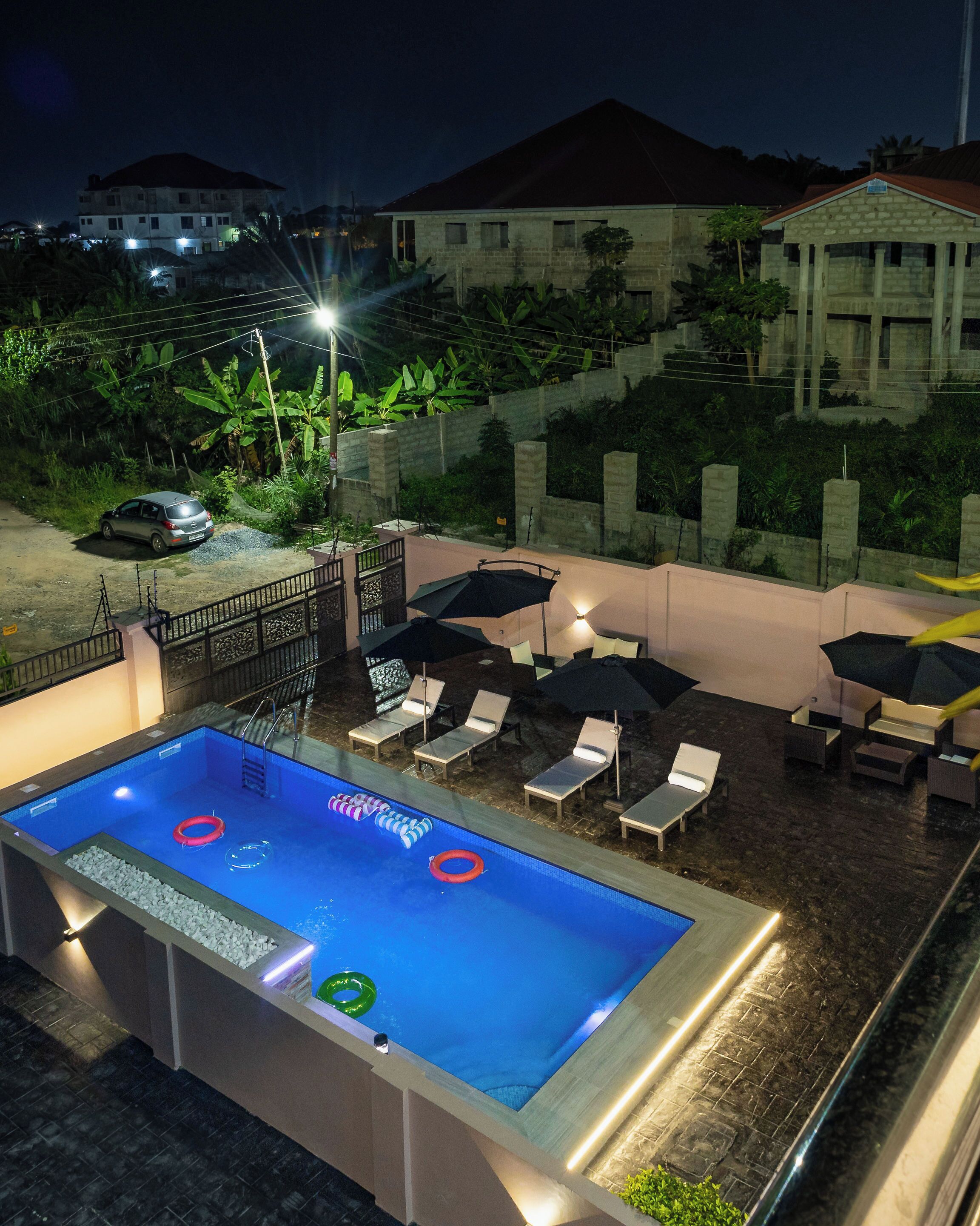 A swimming pool with lounge chairs and umbrellas, surrounded by a concrete wall and vegetation.