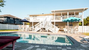 A two-story house with a swimming pool, a covered patio with outdoor furniture, and a white fence.