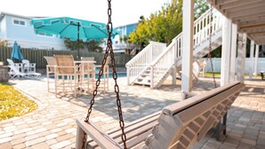 A wooden swing with metal chains, a white staircase, and outdoor furniture including chairs and tables.