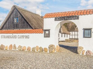 Ein rustikales Gebäude mit dem Schild "Strandgård Camping", einem Strohdach und einem Steinweg, der zu einem Bogen führt.
