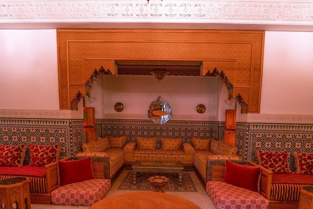 A traditional Moroccan interior with a sofa set, patterned cushions, and a decorative mirror.