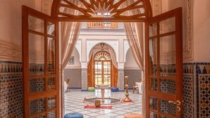 Une arche ouverte mène à une cour intérieure agrémentée d’une fontaine, de carreaux décoratifs et de meubles de style traditionnel.