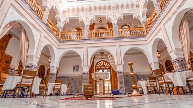 Un intérieur agrémenté d’une fontaine centrale, d’arcades et d’un balcon aux motifs complexes.
