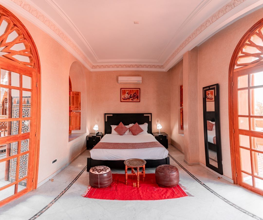 A spacious bedroom with a large bed, two bedside tables, a red rug, and a large mirror.