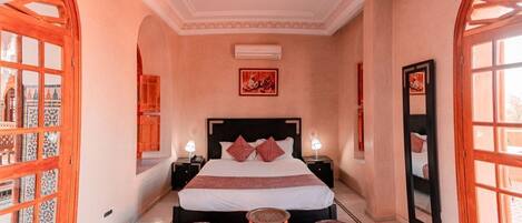 A spacious bedroom with a large bed, two bedside tables, a red rug, and a large mirror.