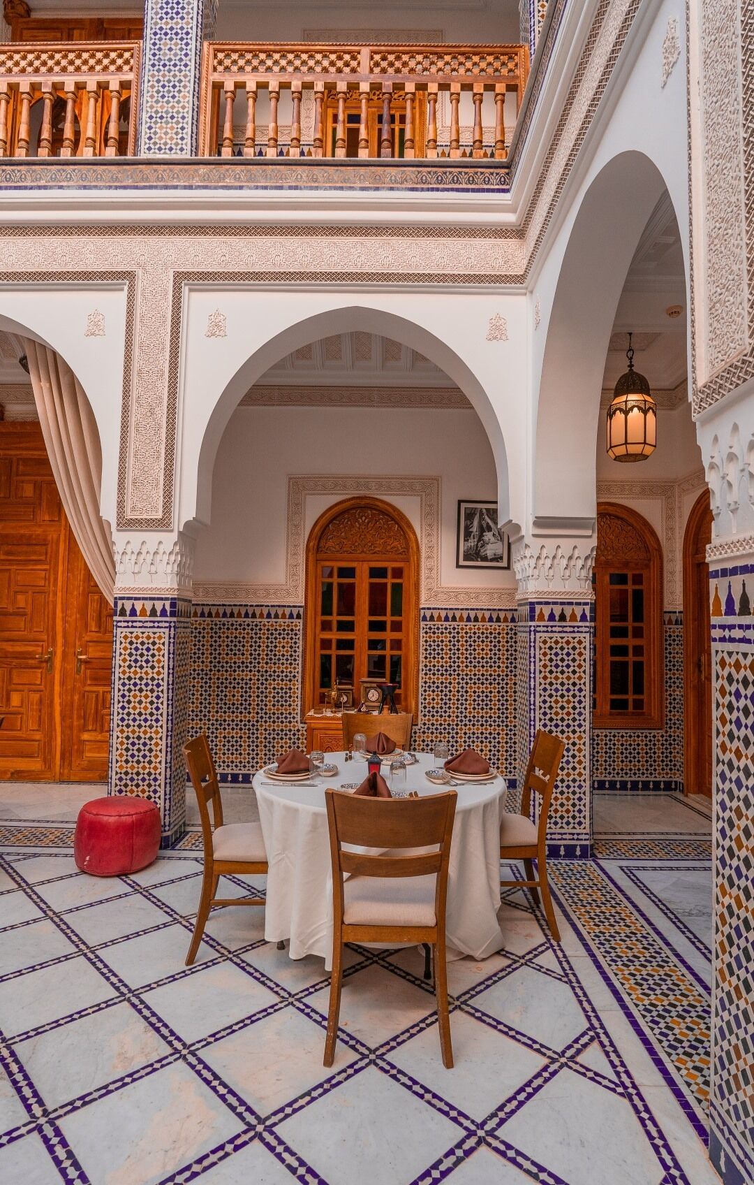 Un espace de restauration intérieur avec une table dressée pour quatre personnes, entouré d’arches et de carreaux décoratifs.