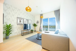 A modern living room with a flat-screen TV, a sofa, a coffee table, and a balcony with a view.