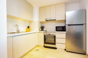 A compact kitchen with a stainless steel refrigerator, a microwave, a stove, and a sink.
