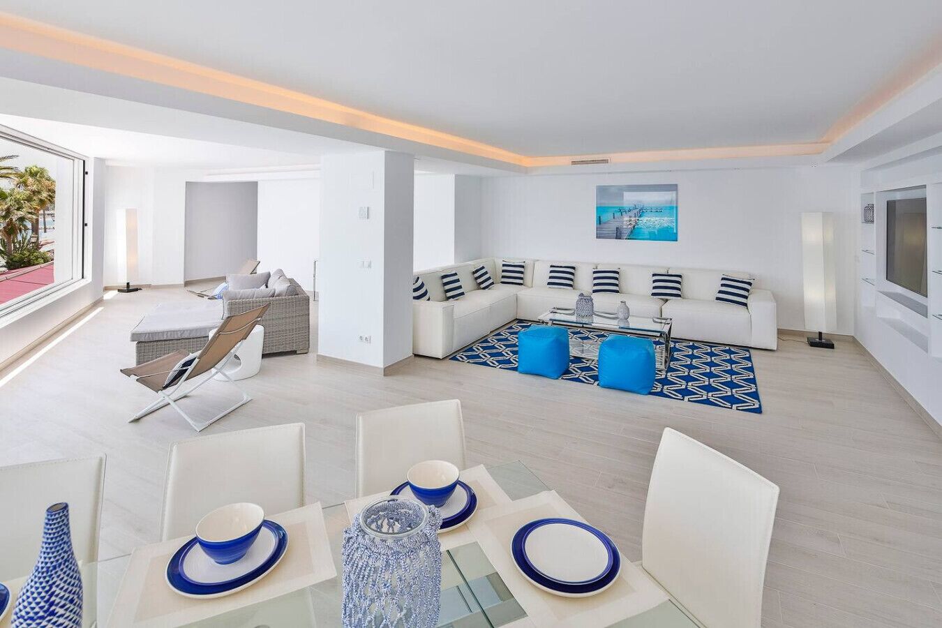 Ein modernes Wohnzimmer mit einem weißen Sofa, einem Glastisch und einem blauen Teppich mit Muster.
