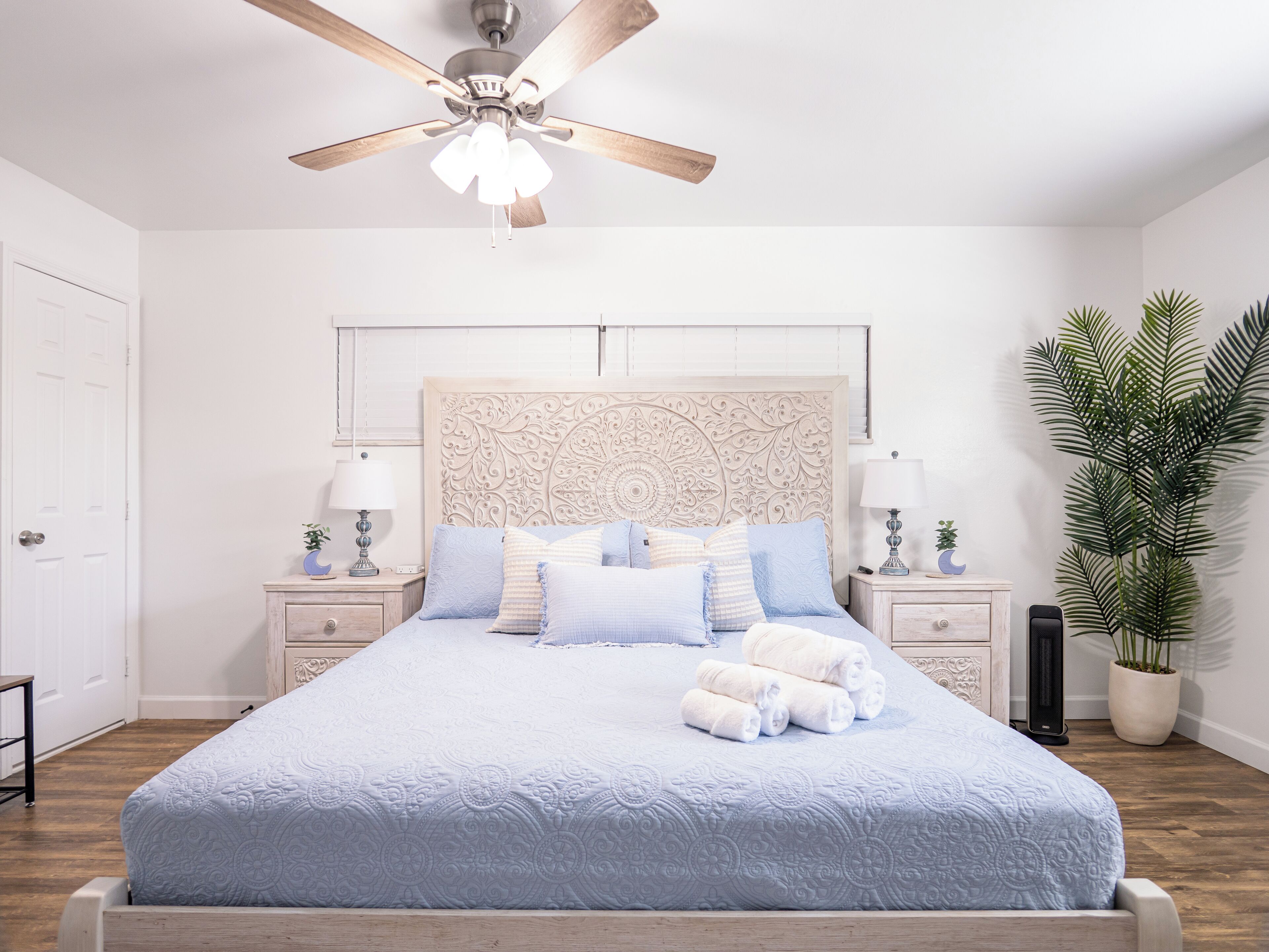Une chambre à coucher avec un lit, des tables de chevet, un ventilateur de plafond et une plante en pot.