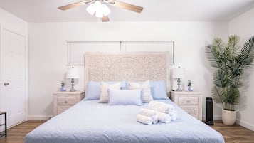 Une chambre à coucher avec un lit, des tables de chevet, un ventilateur de plafond et une plante en pot.