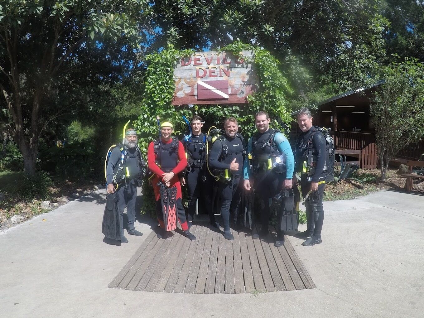 A group of divers standing in front of a wooden sign with the text "DEVIL'S DEN".
