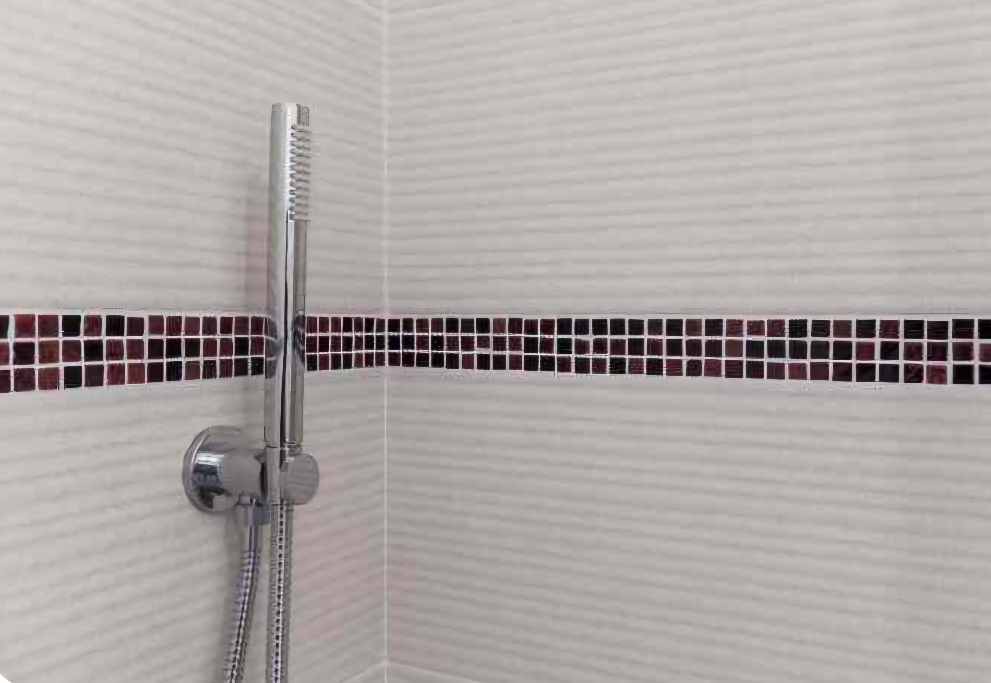 Une douche avec un robinet chromé et un mur carrelé.