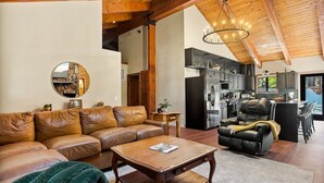 A spacious living room with a leather sofa, a wooden coffee table, and a black leather chair. A kitchen with modern appliances is visible in the background.