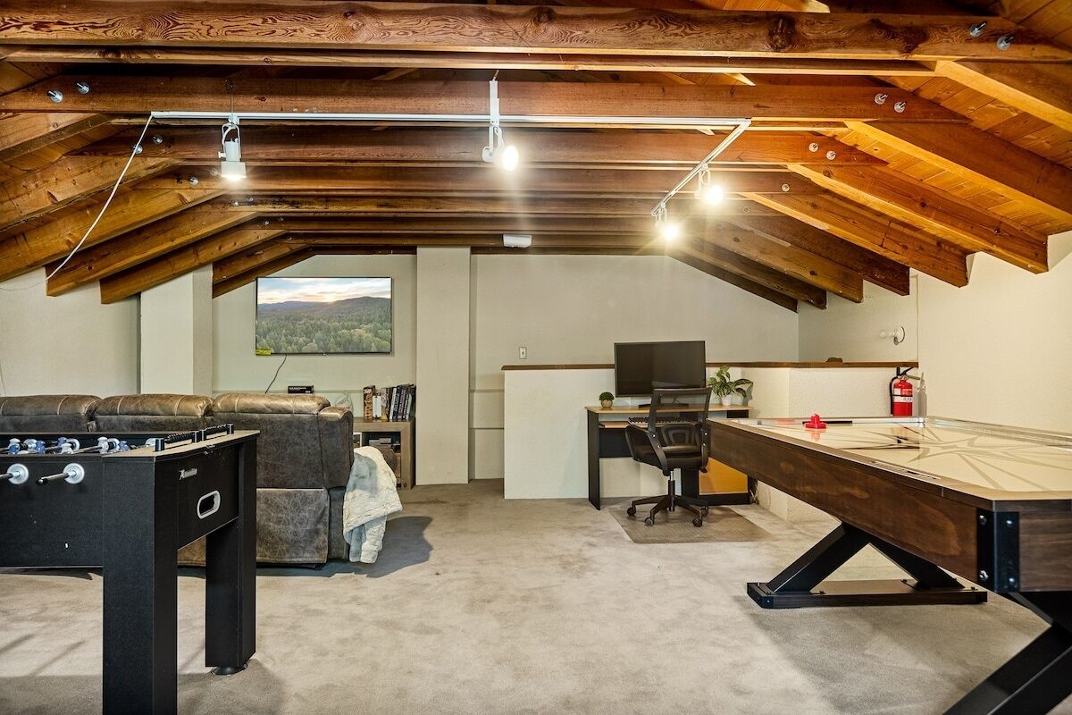Ein Loft-Zimmer mit hohen Decken, freiliegenden Holzbalken, einem Kicker, einem Billardtisch, einem Schreibtisch mit Computer und einer Couch.