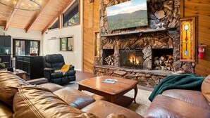A cozy living room with a stone fireplace, leather furniture, and a television mounted on the wall.