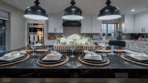 A modern kitchen with a central island, black countertops, and three pendant lights. - 7BR/4BATH Escape w/HEATED Pool, Billiards, Arcade Room, Hot Tub & Mini Golf (Peoria)