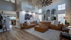 A spacious living room with a large brown sectional sofa, a wooden coffee table, and a patterned rug. There are multiple windows providing natural light, and a ceiling fan is visible. - 7BR/4BATH Escape w/HEATED Pool, Billiards, Arcade Room, Hot Tub & Mini Golf (Peoria)