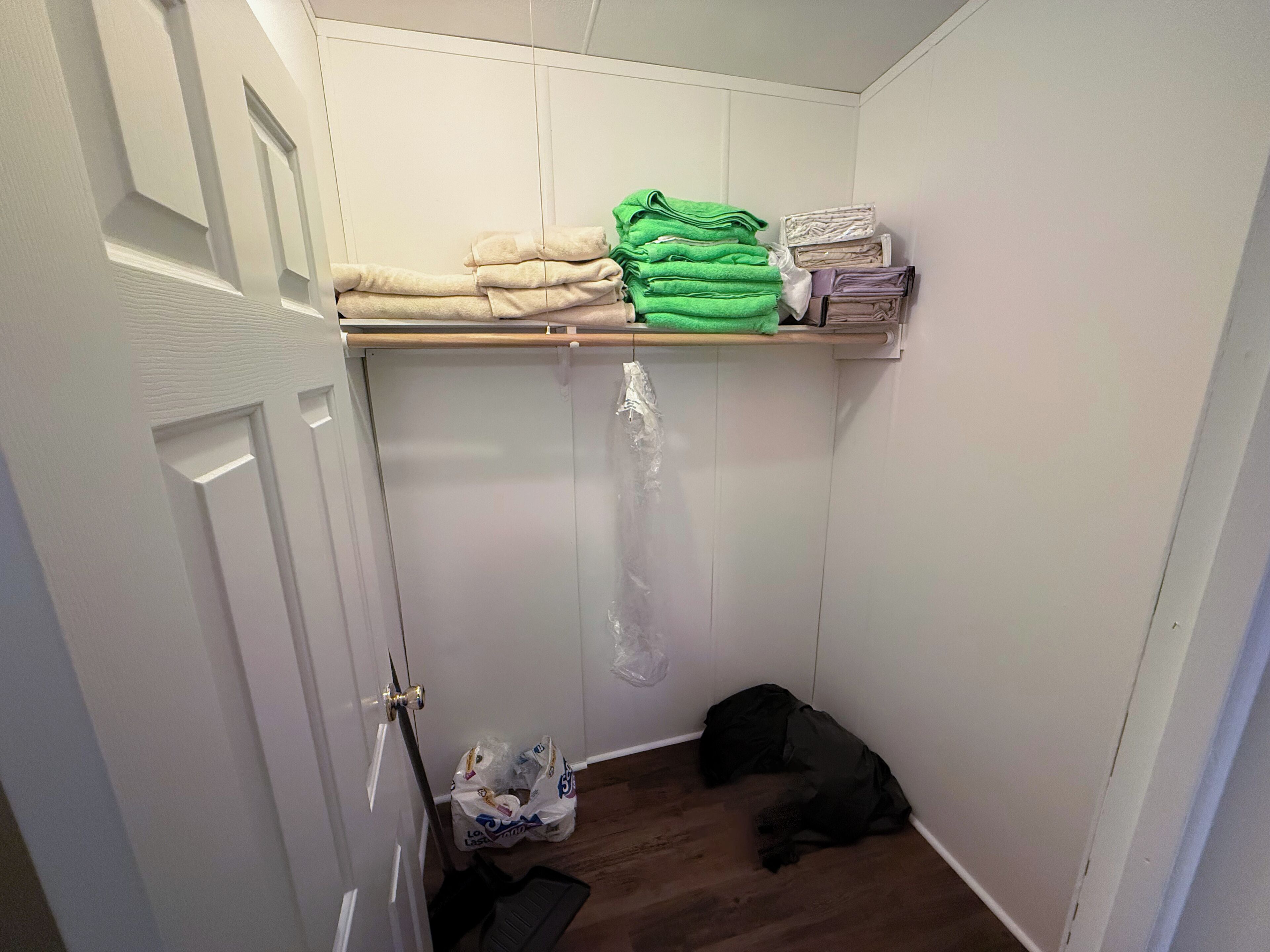 A closet with folded towels and a plastic bag on the floor.