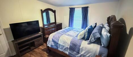 Un dormitorio con cama, televisión, cómoda y ventana con cortinas.