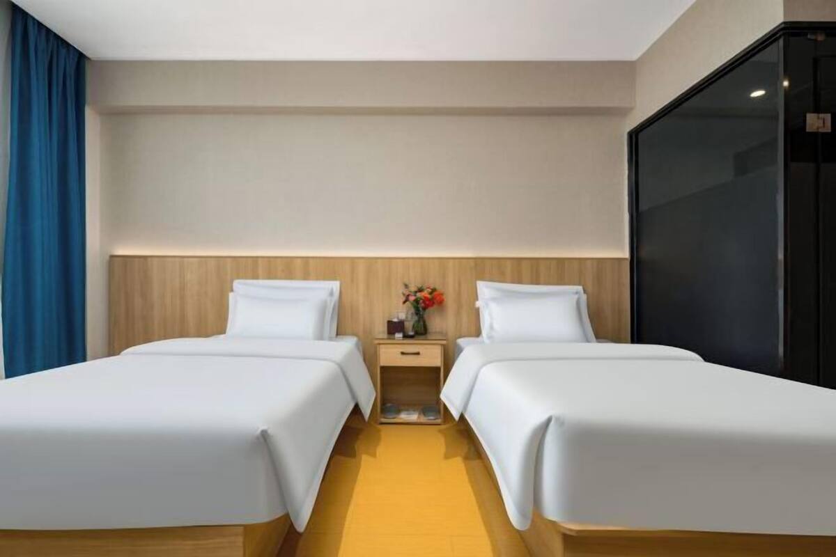 Une chambre d’hôtel avec deux lits, une tête de lit en bois, une table de chevet ornée d’un vase de fleurs et une grande fenêtre.