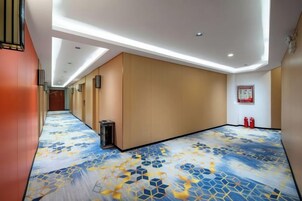 Pasillo de hotel con alfombra estampada, iluminación empotrada y un extintor en la pared.