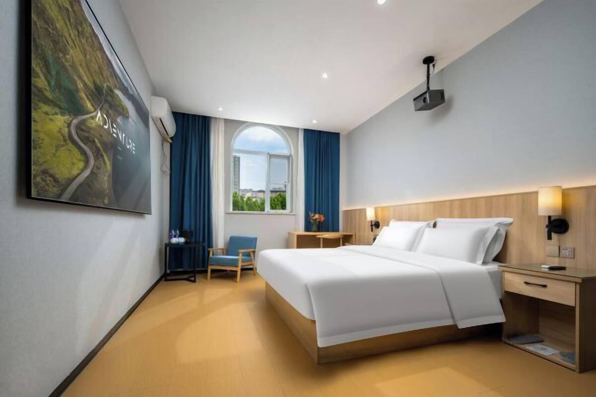 Une chambre d’hôtel moderne dotée d’un grand lit, d’un bureau, d’une chaise, d’une fenêtre avec vue et d’un téléviseur fixé au mur.