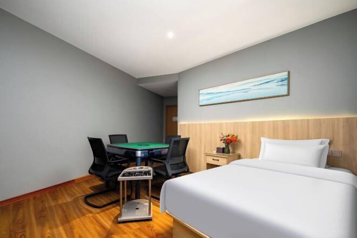 Une chambre d’hôtel avec un lit, un bureau doté d’un plateau recouvert de feutre vert, une chaise, une balance et un tableau encadré accroché au mur.