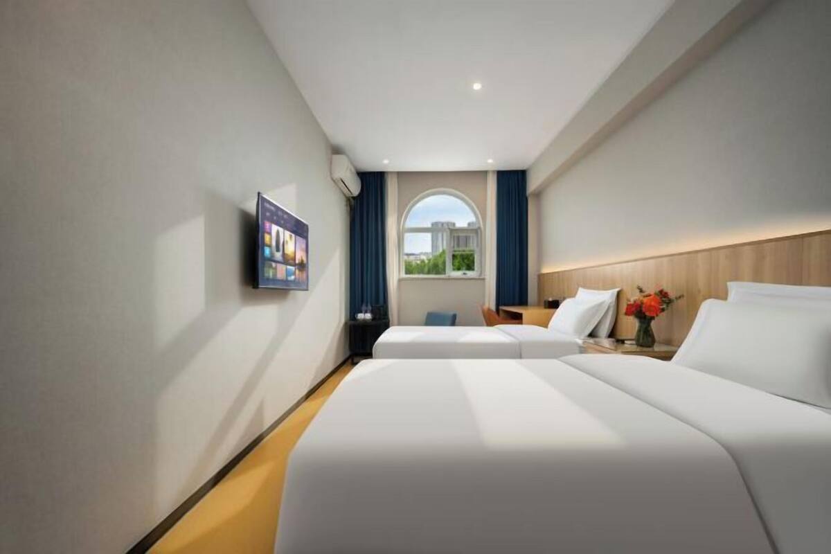 Une chambre d’hôtel avec deux lits, une télévision, une fenêtre avec des rideaux et une tête de lit en bois.