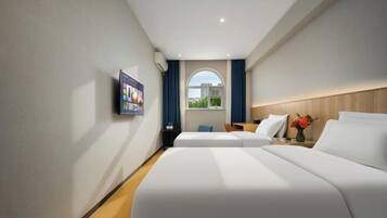 Una habitación de hotel con dos camas, televisión, ventana con cortinas y cabecero de madera.