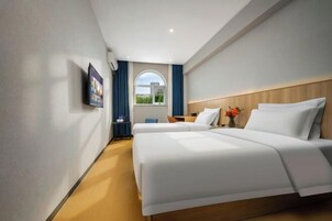 Habitación de hotel con dos camas, un televisor fijado a la pared, una ventana con cortinas y vistas a zonas verdes.