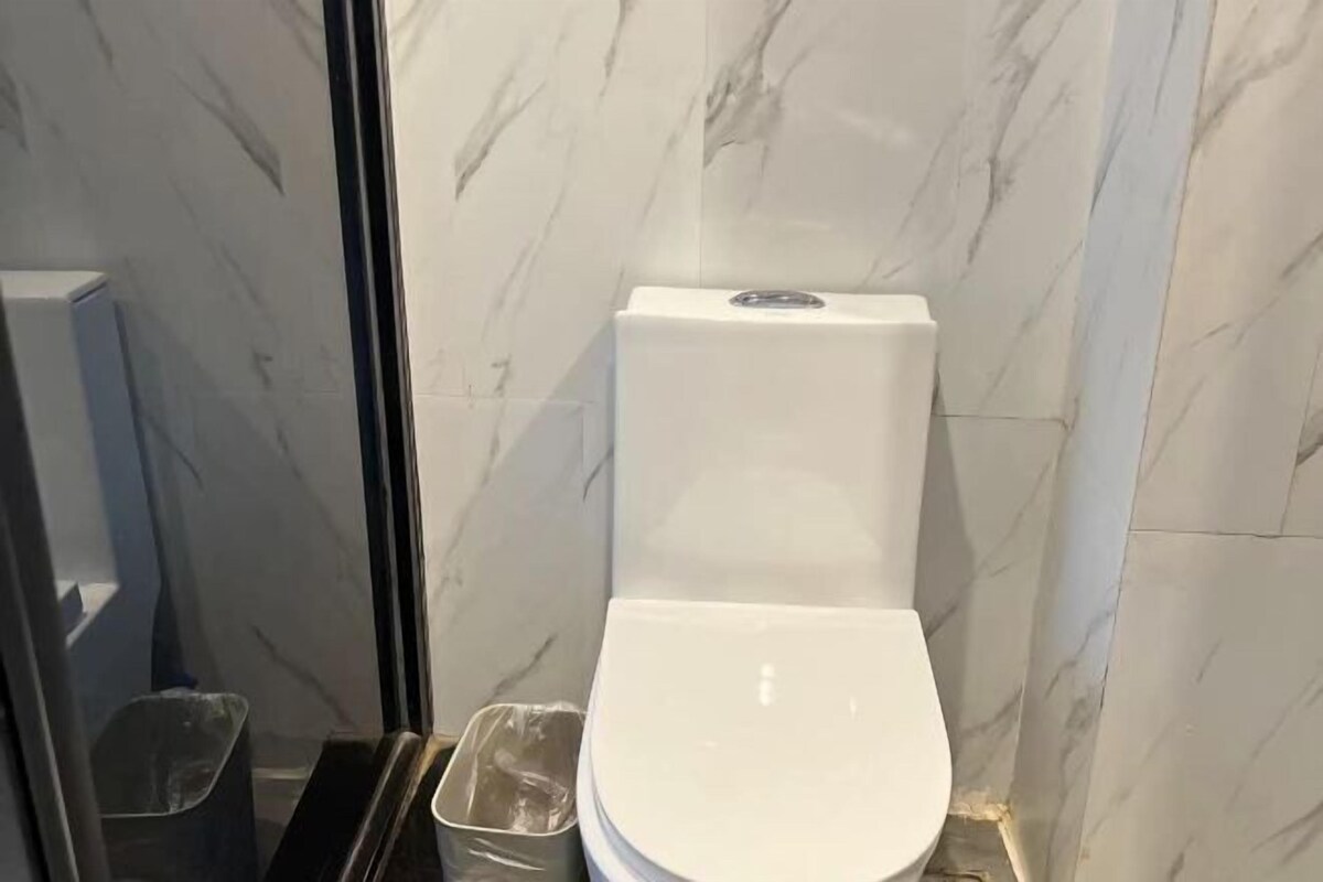 A bathroom with a white toilet, a trash bin, and marble walls.