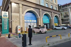 A building with multiple arches and a parking area with cars. - Jingman Light Luxury Hotel (Shangqiu Experimental Middle School High-speed Railway Station) (Shangqiu)