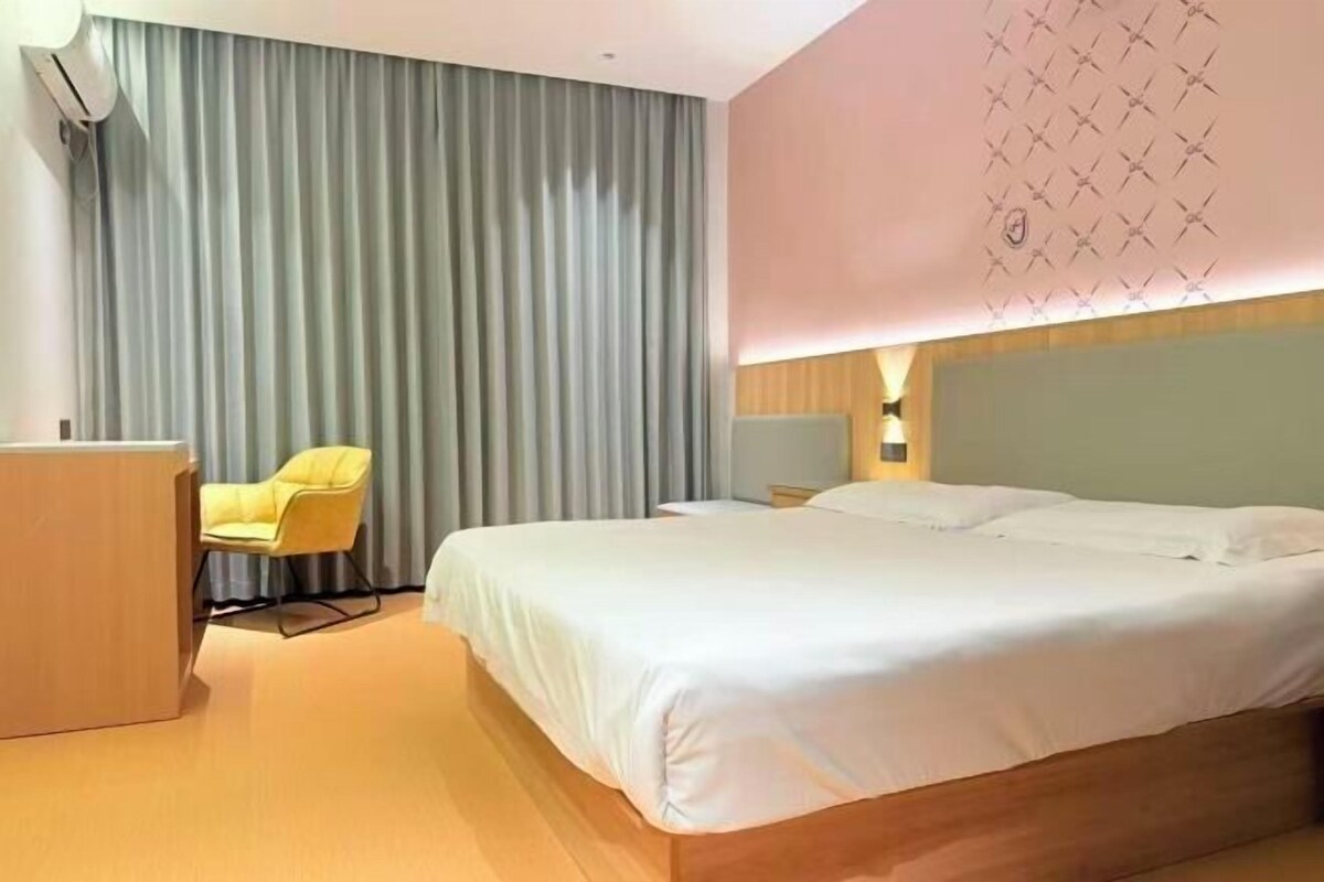 A hotel room with a bed, a desk, a chair, and a curtain.