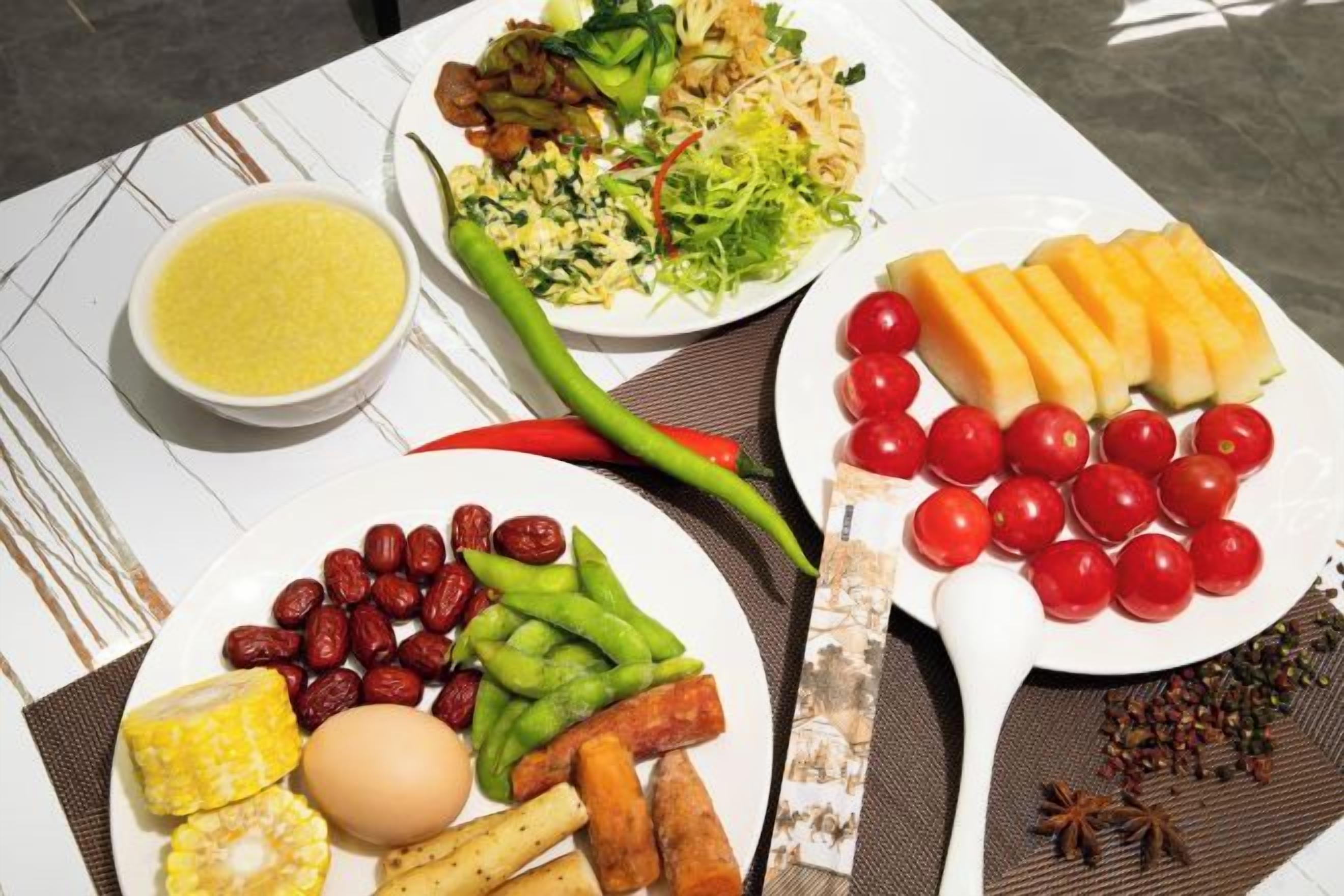 Una mesa con diversos alimentos, entre ellos una ensalada, tomates y un tazón de sopa.