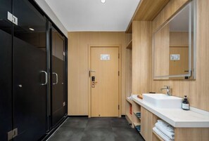 A modern bathroom with a wooden door, a white sink, and a mirror.