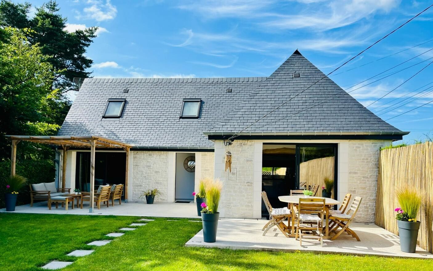 Et hus med skråt tag, en overdækket terrasse med udendørs møbler og en facade af natursten.