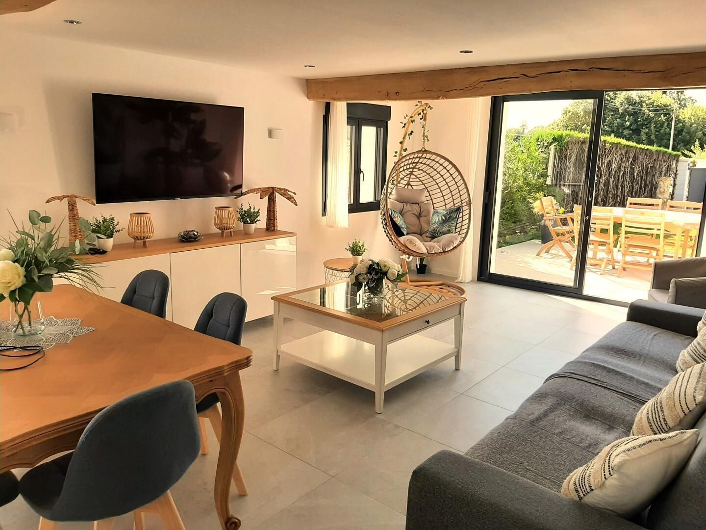Een moderne woonkamer met een houten eettafel, een bank, een hangstoel en een aan de muur bevestigde televisie.