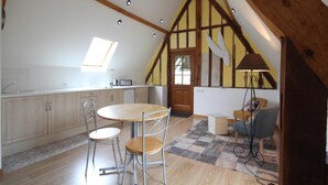 A kitchen with a wooden ceiling, a dining area with a table and chairs, and a small seating area with a lamp.