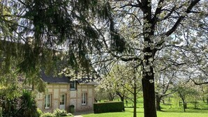 A stone house with a paved pathway leading to the entrance, surrounded by well-maintained grass and trees.