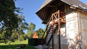 A rustic building with a wooden staircase leading to a loft area, surrounded by greenery and a clear sky.