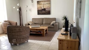A living room with a sofa, two wicker chairs, a coffee table, and a TV stand with a lamp.