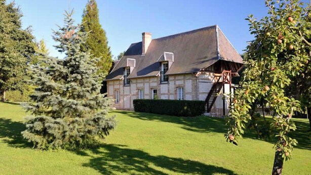A large house with a sloped roof, surrounded by a well-maintained lawn and trees.