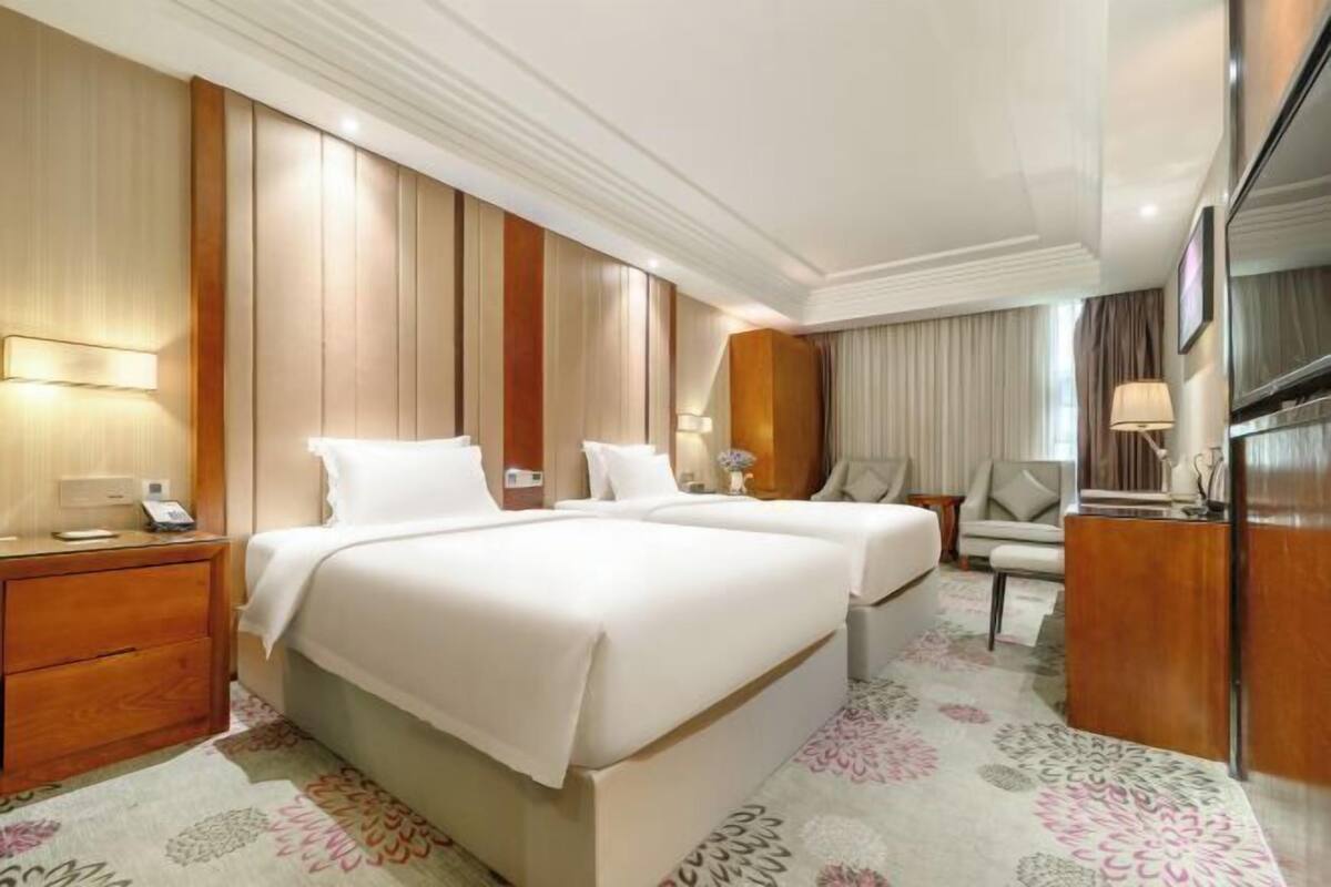 A hotel room with a large bed, bedside tables, a desk, a chair, and a television.