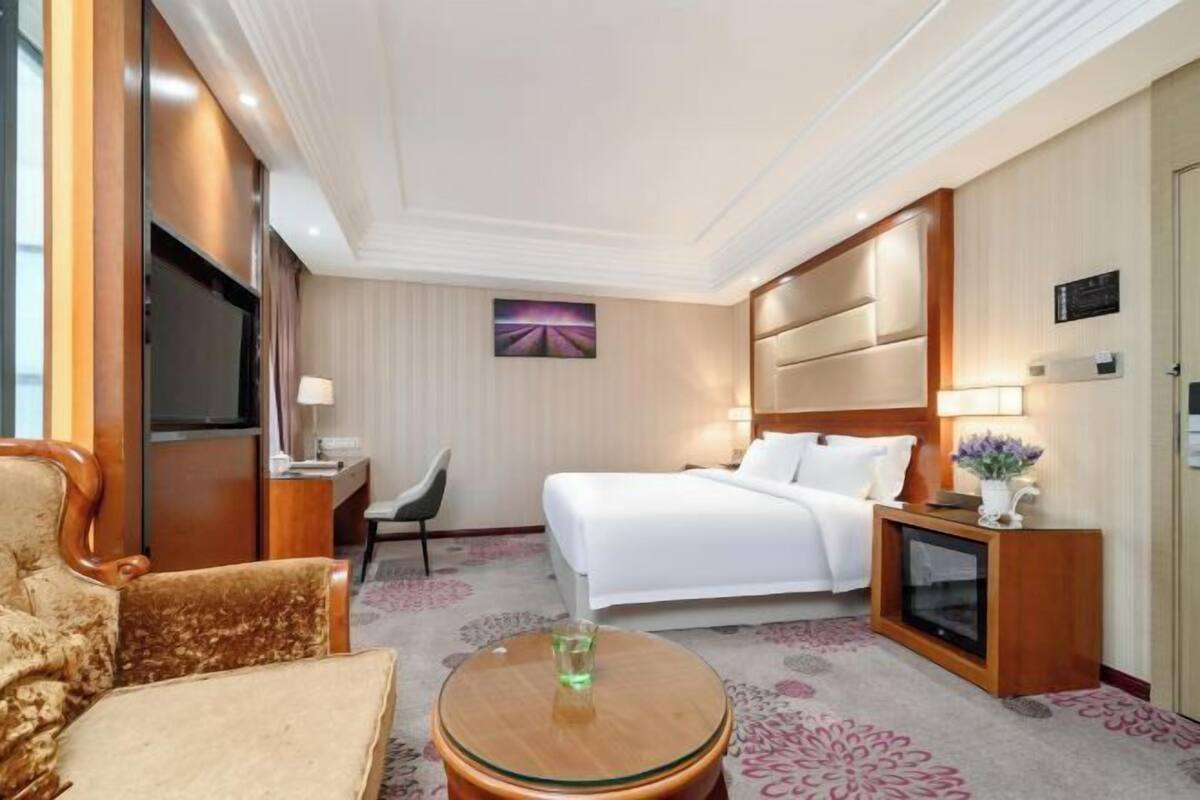 A hotel room with a bed, a desk, a television, a chair, and a round table.