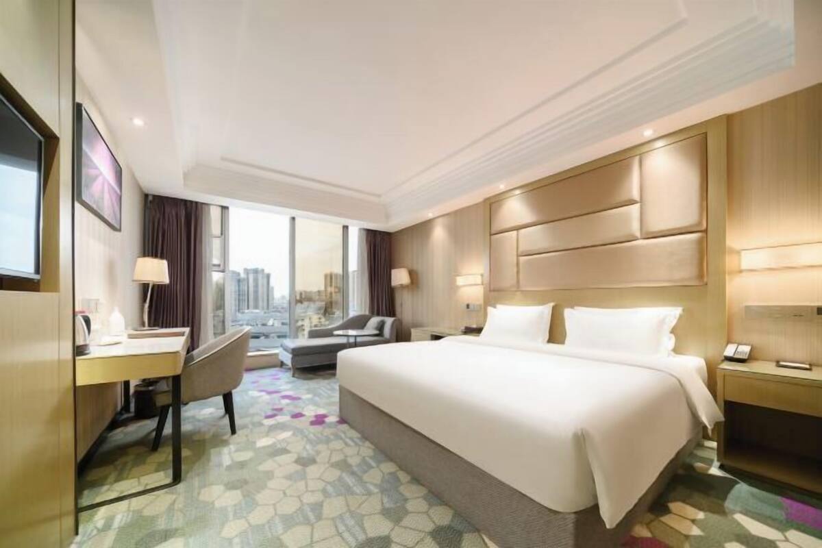 A hotel room with a large bed, a desk, a chair, and a view of the city.