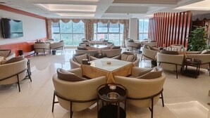 A spacious hotel lobby with multiple seating areas, including round tables and sofas, large windows offering a view of the outdoors, and a flat-screen TV mounted on the wall. - Lavande Hotel (Suining Heping West Road) (Suining)