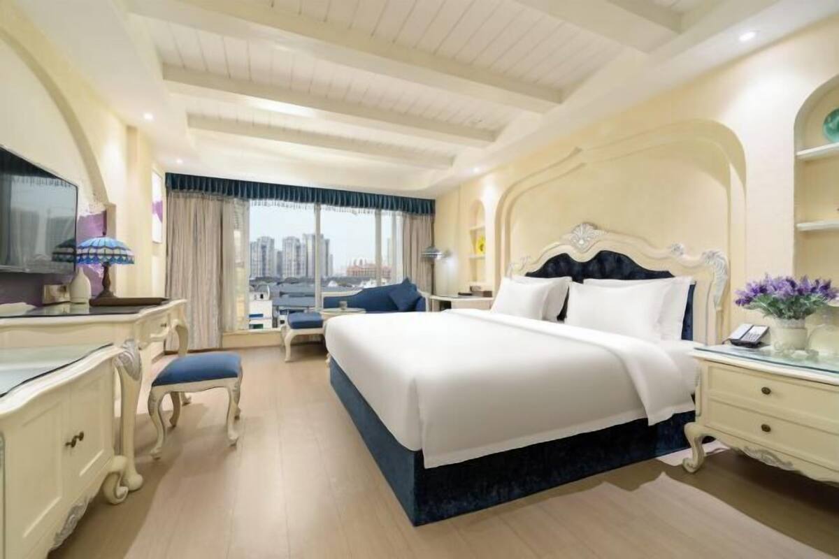 A hotel room with a large bed, a desk, a chair, and a view of the city.